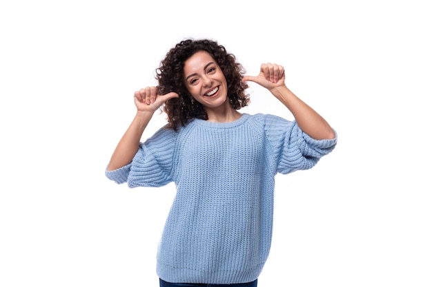 Portrait of a slim young pretty lady with black curly hair dressed in a light blue sweater