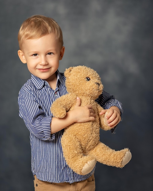 Portrait of a small boy child with a teddy bear Little kid and favorite toy on grey background Happy childhood concept A gift for a birthday or other holiday