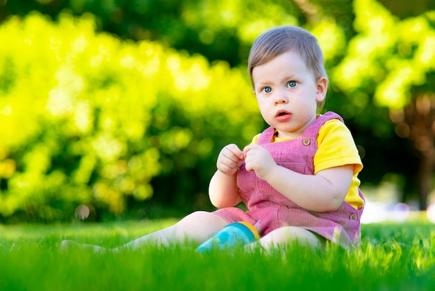 Portrait of a small surprised girl child pensive kid sits in the park on the grass outside