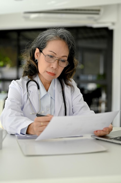 Portrait smart asian aged female doctor focusing on reading a\
medical research case