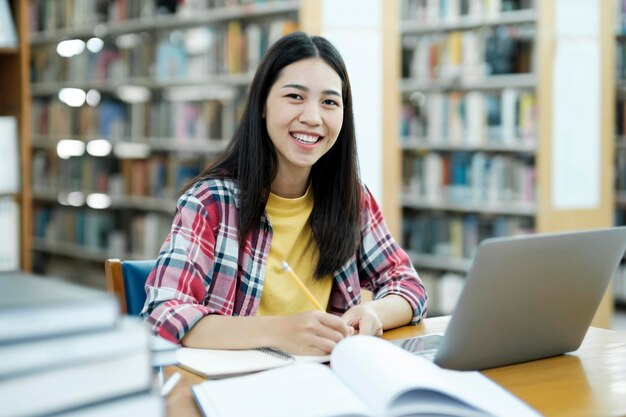 Photo portrait of a smart beautiful asian girl studing and reading text books smiling looking at camera