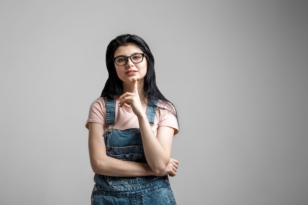 Portrait of smart beautiful brunette girl in eyeglasses with natural make-up, on grey background.