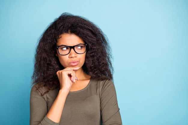 Portrait of smart intelligent clever dark skin girl in spectacles think ponder have thoughts about her business project feel unaware unsure wear stylish outfit isolated over blue color wall 