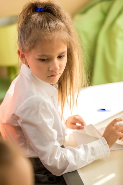 Portrait of smart schoolgirl sitting at desk in bedroom