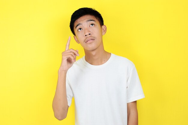 Portrait of smart young Asian man thinking and look up. Smart young Asian man wearing white t-shirt thinking and look up, on yellow background