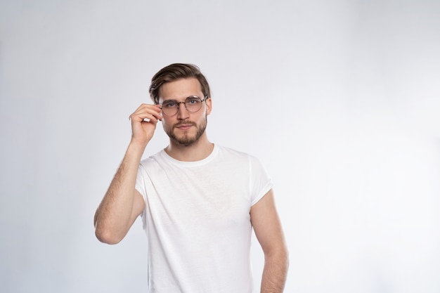 白い背景に立っている眼鏡のスマートな若い男の肖像画。
