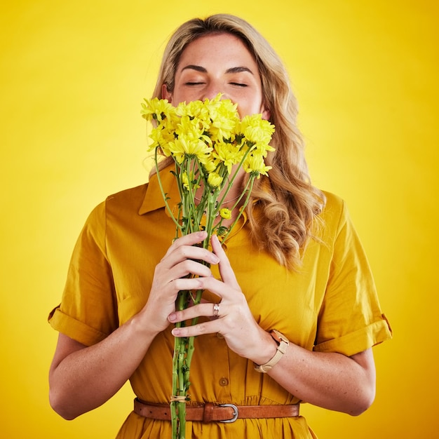 Portrait smelling and woman with flowers in studio isolated on a yellow background Floral bouquet and person sniff aroma or scent with female model holding natural plants and fresh flower