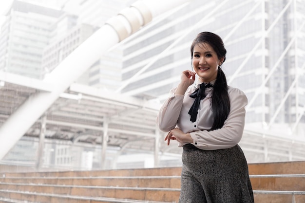 Portrait smile Asian office worker girl with crossed arms at outdoor and copy space. Smiling happy Thai businesswoman with city background.