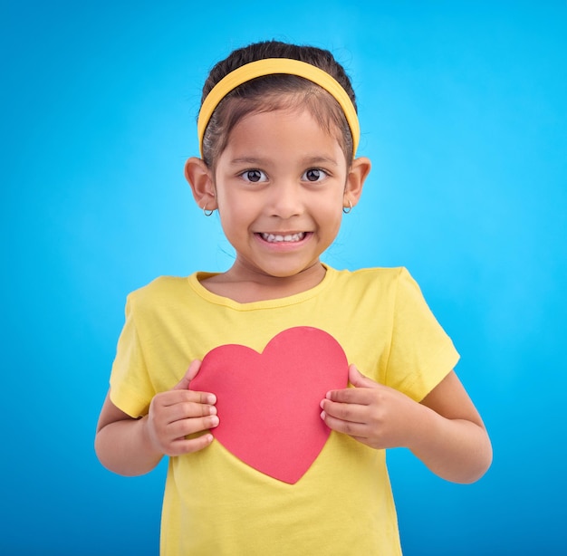 Portrait smile and girl with heart cutout joy and cheerful against a blue studio background Face Indian female child and kid with love symbol excited and young person with sign mockup and happy