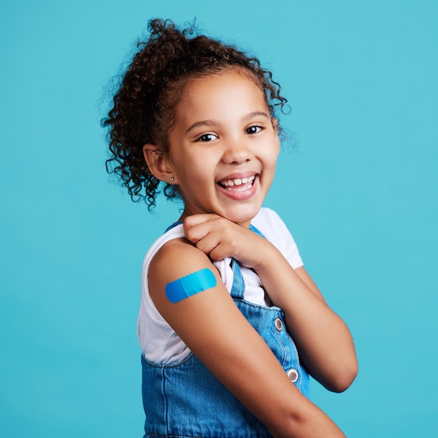 Photo portrait smile and girl with plaster wellness and safety with kid against a blue studio background face young person and female child with happiness band aid and vaccine with protection and care