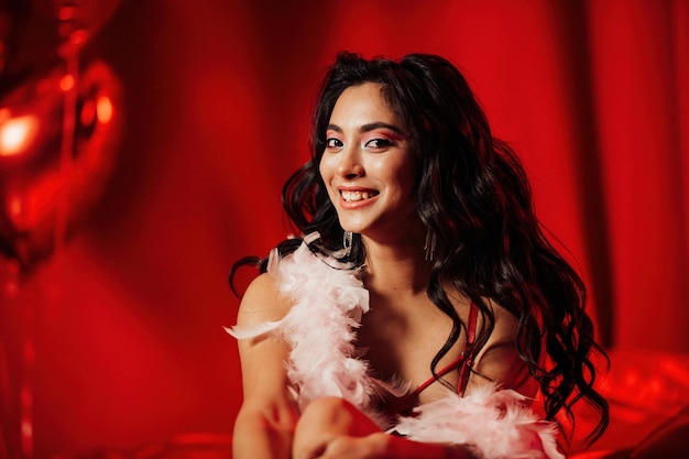 Photo portrait of smile sexy asian girl glam makeup in lingerie and feather boa among red shiny balloons