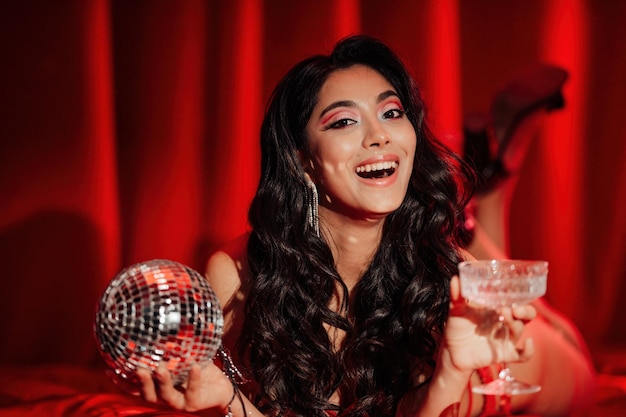Портрет улыбающейся сексуальной азиатской девушки с гламурным макияжем в красном кружевном белье, лежащей на кровати в день святого валентина