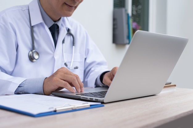 Portrait smiling 40s asian doctor working on laptop computer telemedicine EHRs Electronic Health Records system concept