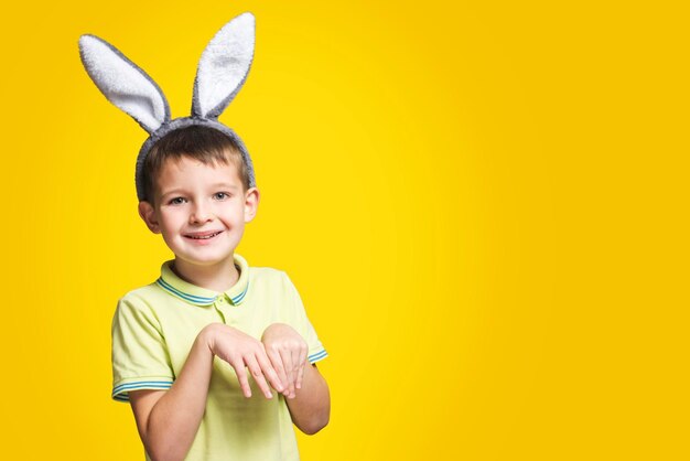 黄色い背景にウサギの耳をかぶった笑顔の可愛い小さな男の子の肖像画