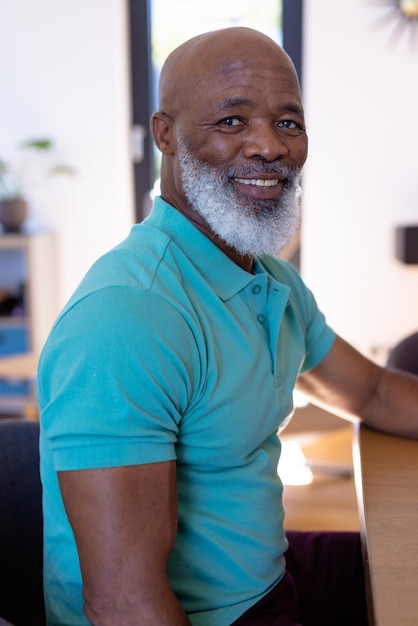 Portrait of smiling african american bald senior man sitting at dining table in nursing home. Beard, unaltered, support, assisted living and retirement concept.