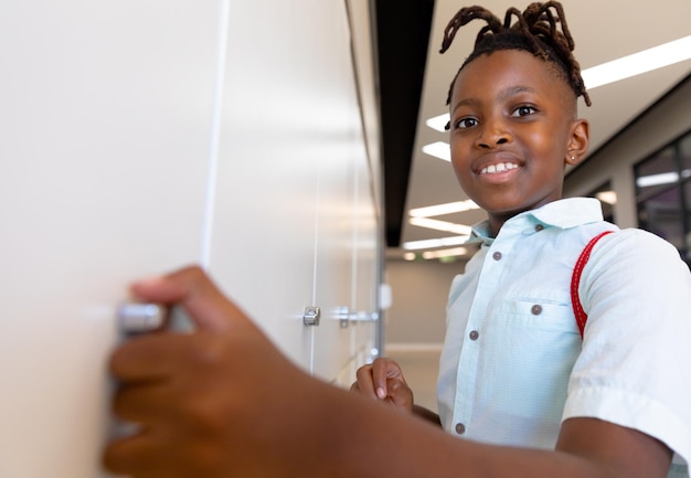 Portrait of smiling african american elementary schoolboy standing by locker in school