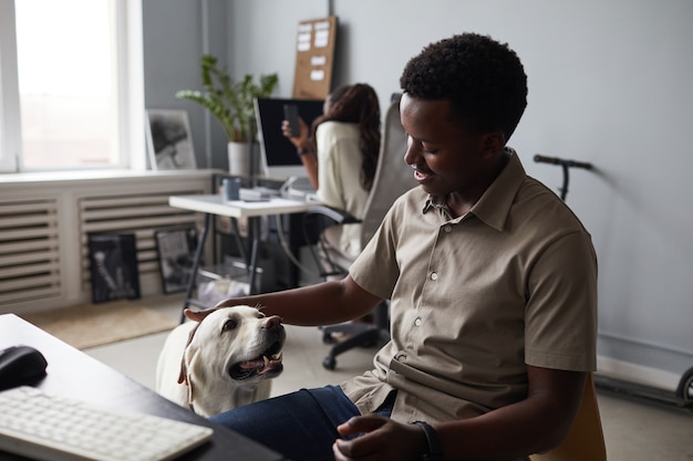 사무실에서 일하는 동안 개를 쓰다듬는 웃고 있는 아프리카계 미국인 남자의 초상화, 애완동물 친화적인 작업 공간