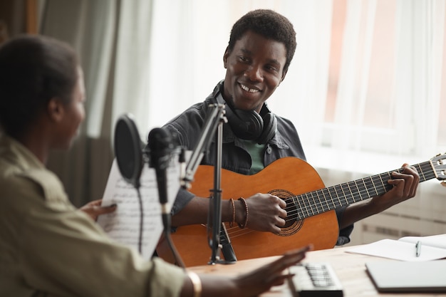 Portrait of smiling African-American man playing guitar while recording music at home, copy space