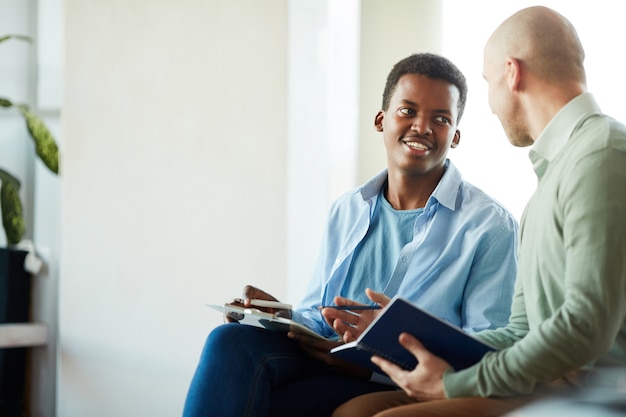 Portrait of smiling African-American man talking to manager during business internship in office, copy space