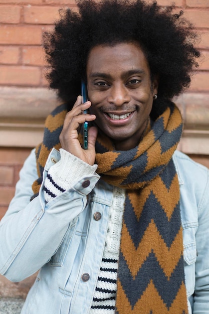 Portrait of smiling African American man with modern look and afro hairstyle talking on phone outdoors.