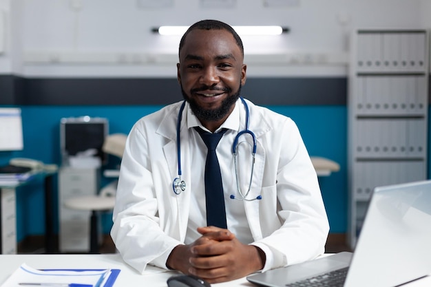 Portrait of smiling african american specialist doctor sitting at desk in hospital