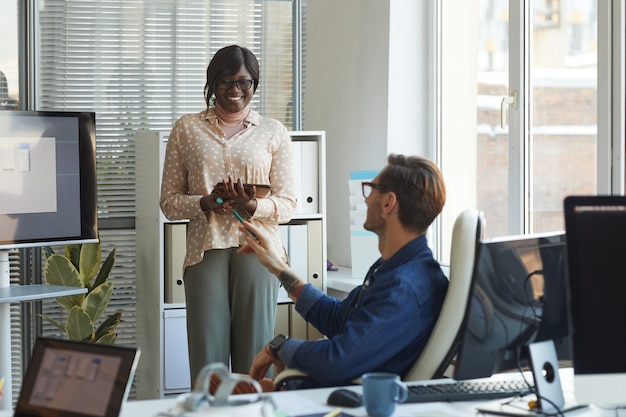 Portrait of smiling African-American woman giving presentation at meeting in modern office with colleagues asking questions, copy space