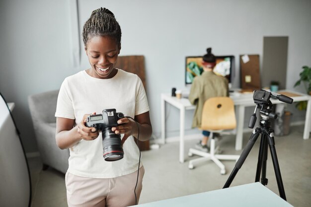 Portrait of smiling African American woman holding camera while working in photo studio copy space