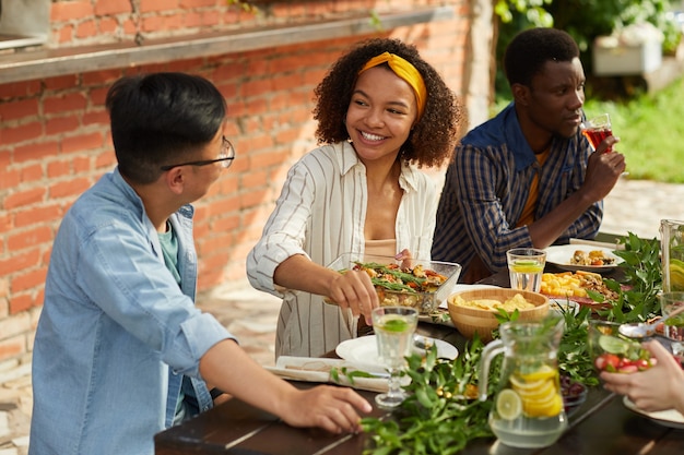 여름 파티에서 야외에서 친구 및 가족과 함께 저녁 식사를 즐기면서 감자 접시를 들고 웃는 아프리카 계 미국인 여자의 초상화