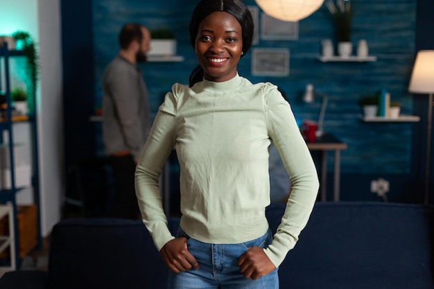 Portrait of smiling african american woman looking into camera enjoying hanging out together celebrating night party with multi-ethnic friends. Group of people drinking beer, eating snack at home