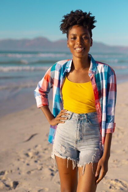 Portrait of smiling african american young woman with short hair standing at beach against blue sky