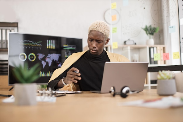 Portrait of smiling african young male office manager in yellow suit writing financial report