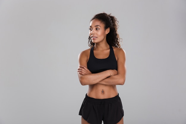 Photo portrait of a smiling afro american sportswoman isolated over gray wall, standing, looking away