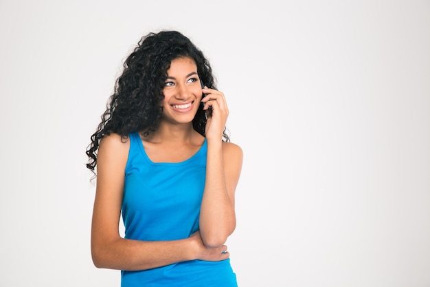 Ritratto di una donna afroamericana sorridente, parlando al telefono e distogliendo lo sguardo isolato su un muro bianco