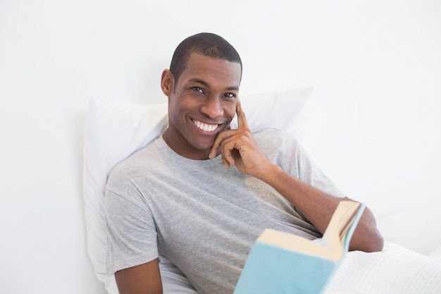 Portrait of a smiling Afro man with a book in bed