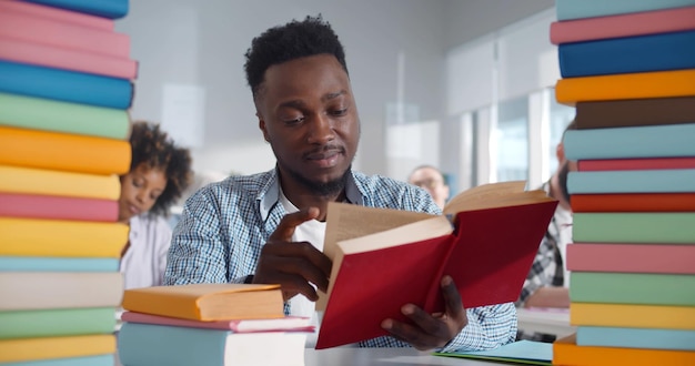 Portrait of smiling afroamerican young man with pile of books studying in classroom