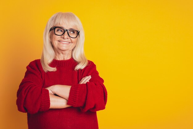 Portrait of a smiling aged woman arms crossed isolated against yellow background