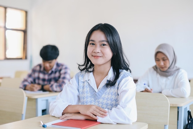 Портрет улыбающейся азиатской студентки, сидящей за столом в классе в университете