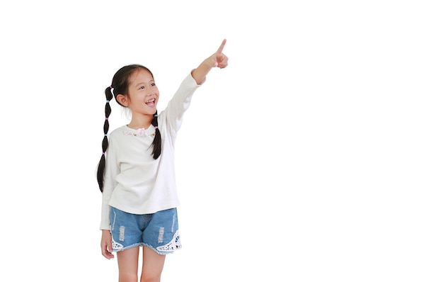 Портрет улыбающейся азиатской маленькой детской девочки указывает указательным пальцем вверх на белом фоне с копией пространства