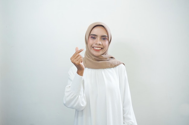 Portrait of smiling Asian Muslim woman showing heart gesture isolated over white background