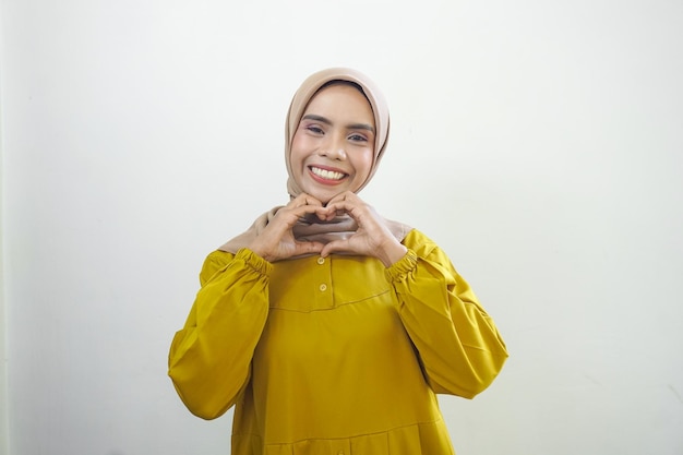 Portrait of smiling Asian Muslim woman showing heart gesture isolated over white background