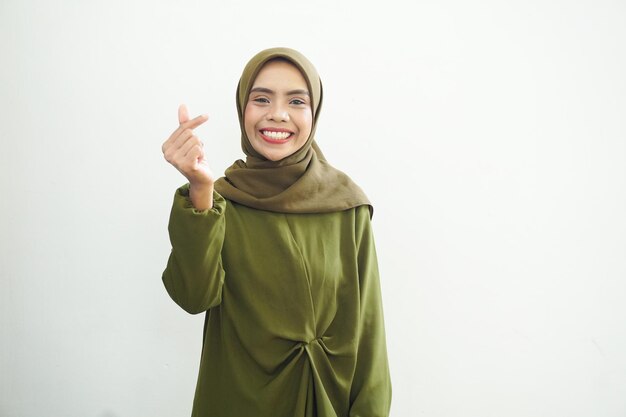 Portrait of smiling Asian Muslim woman wearing green casual dress showing heart gesture