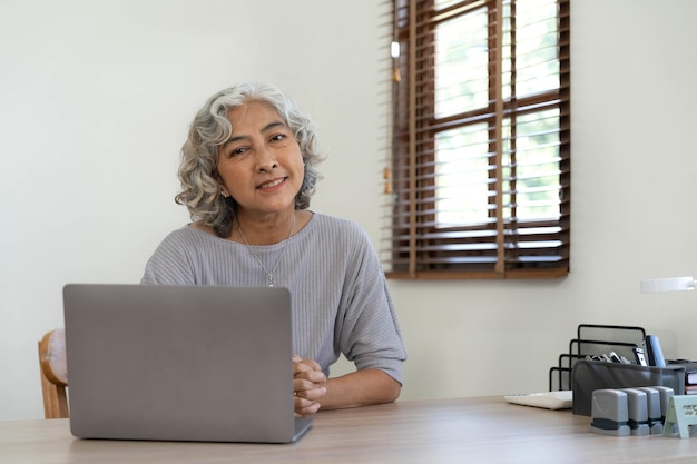 Portrait of smiling asian senior mature middle aged\
businesswoman using laptop working and web surfing on desk