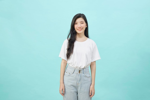 Portrait of a smiling Asian student woman standing looking at camera isolated blue background