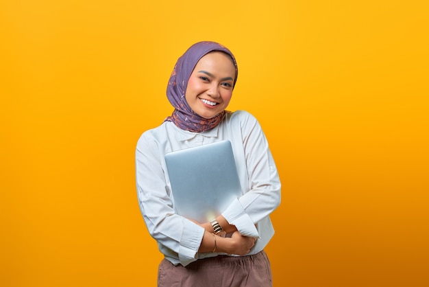 Il ritratto della donna asiatica sorridente porta il computer portatile sopra fondo giallo