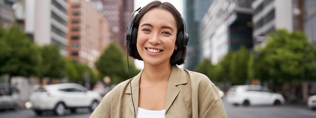 Photo portrait of smiling asian woman in headphones standing in city centre on street looking happy