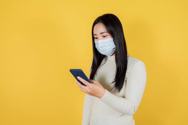 Portrait of smiling asian woman wears using a smartphone on yellow background