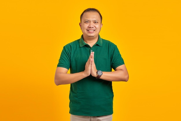 Portrait of smiling Asian young man holding hands pleading over yellow background