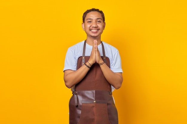 Portrait of smiling Asian young man wearing apron greeting customer with big smile on his face