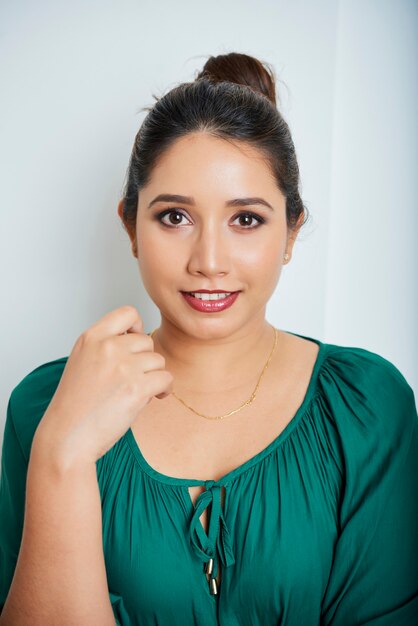 Photo portrait of smiling attractive asian woman in emerald green blouse touching necklace and looking at camera