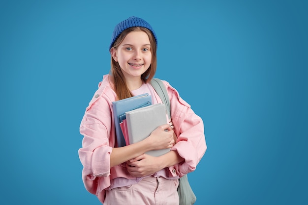 Portrait of smiling attractive girl with braces standing and holding heap of textbooks